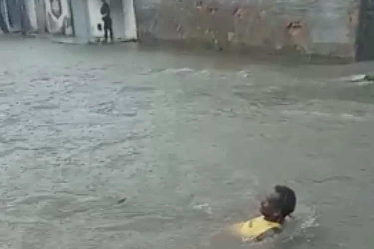 Homem toma banho em rua alagada após fortes chuvas em Guanambi